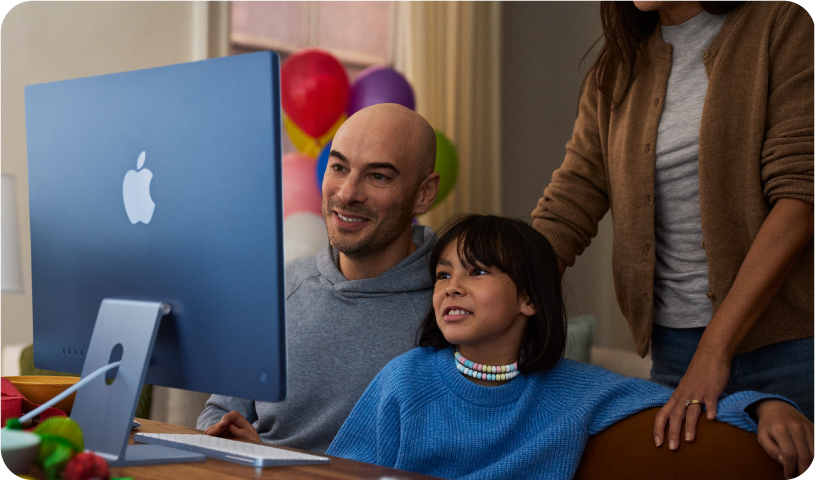 Dois pais e uma criança olhando para um iMac juntos.
