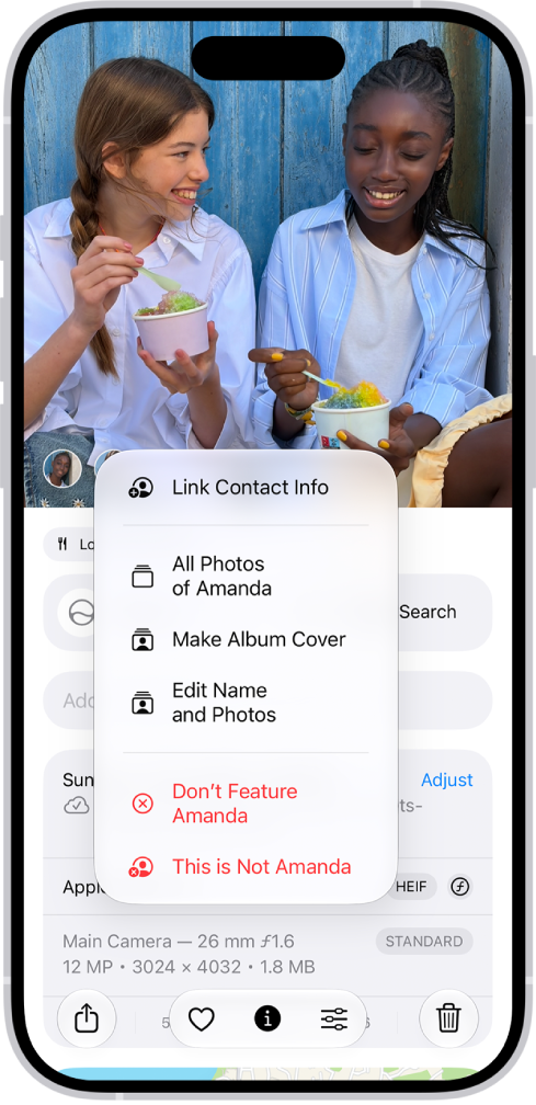 La mitad superior de la pantalla del iPhone mostrando una foto abierta en la app Fotos. En la esquina inferior izquierda de la foto están las caras de las personas que aparecen en la foto. Una de las caras tiene un signo de interrogación al lado de ella. El menú de opciones incluye, de arriba abajo: Todas las fotos, Establecer como foto principal, Editar nombre y fotos y No incluir a esta persona.