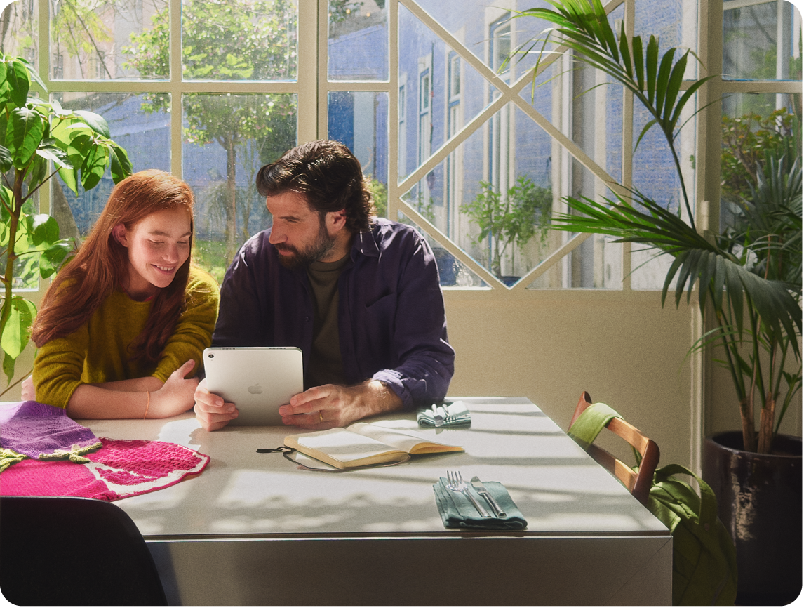 Um responsável e um adolescente sentados à mesa, olhando para um iPad juntos.